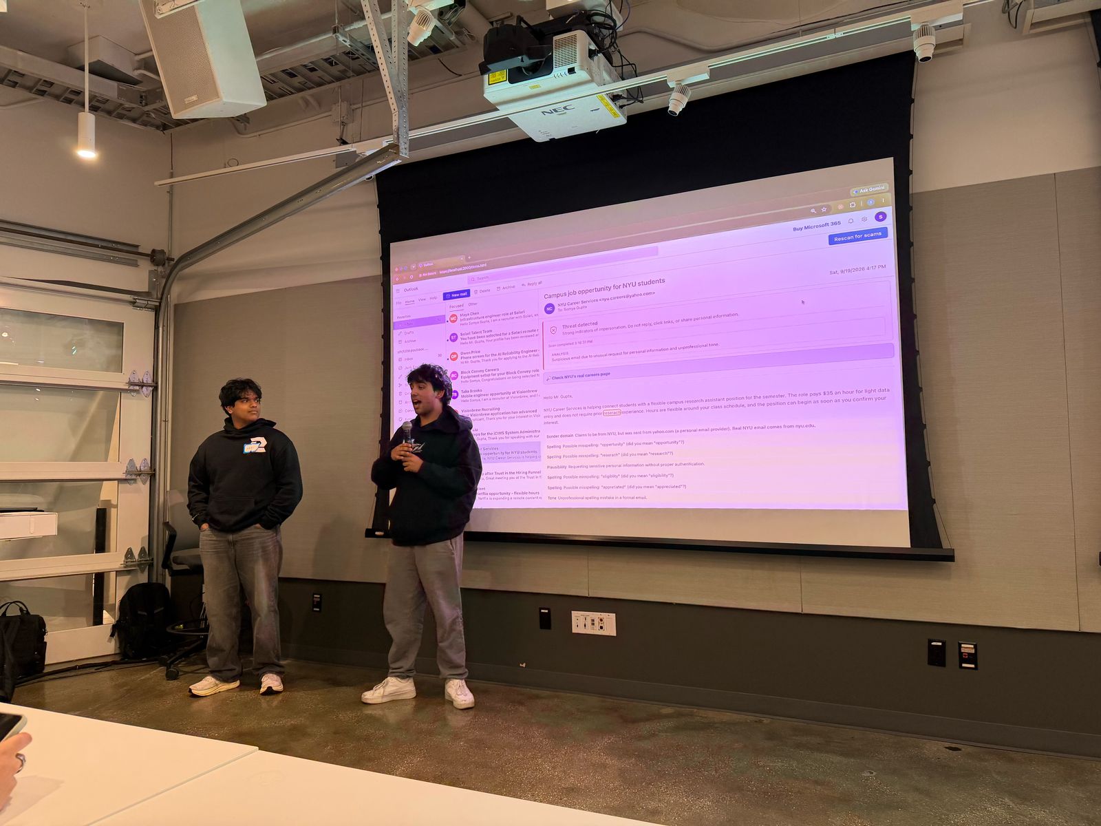Two hackathon participants presenting a demo on a large screen