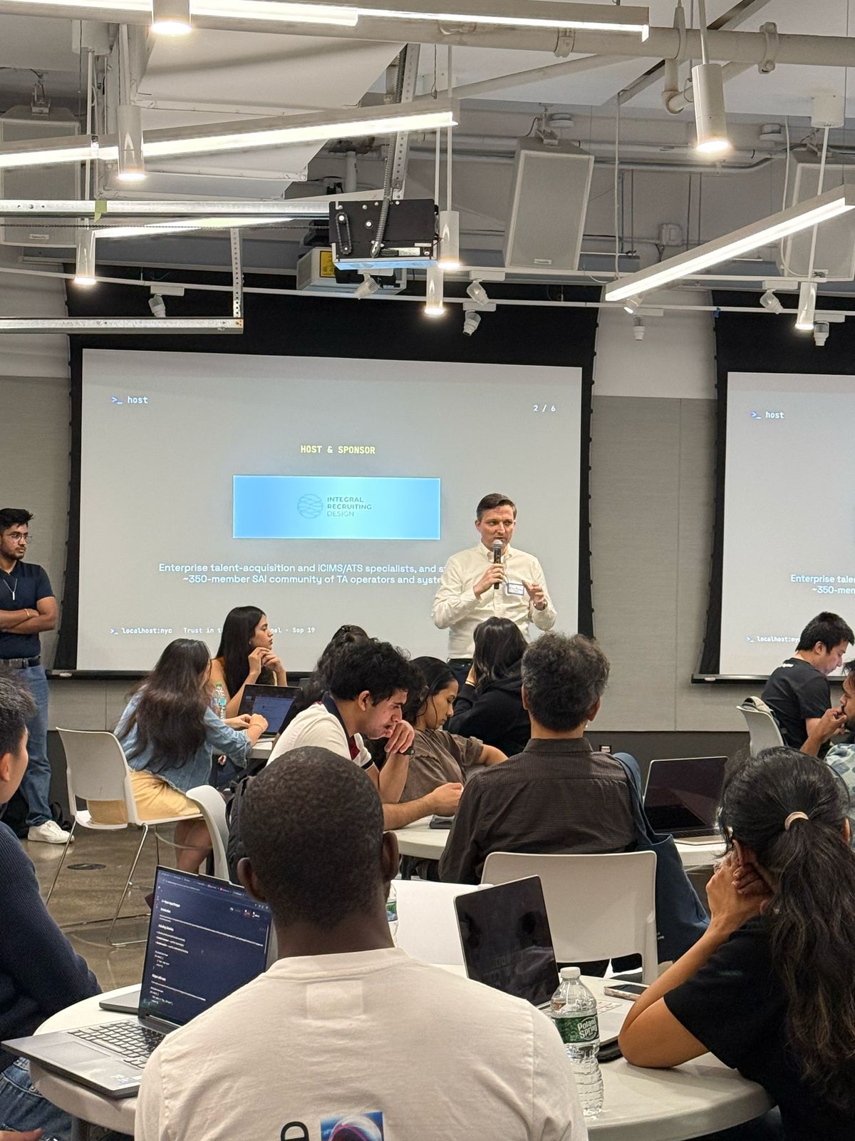 Alex Marcus speaking at the TA Hackathon at NYU, in front of a slide naming IRD as host and sponsor