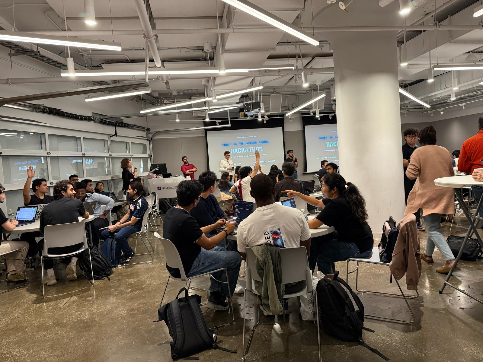The TA Hackathon room at NYU, with participants at tables and HACKATHON on both screens